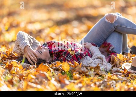 Sorglos schöne Brünette im Park liegend entspannen während sonnigen Herbst Sonnenuntergang. Stockfoto