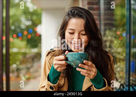 Porträt einer niedlichen jungen asiatischen Frau, die Kaffee auf der Terrasse des Cafés trinkt. Im Freien. Gemütliche Herbstsaison Stockfoto