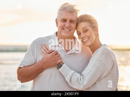 Liebe, Reise und Strandportrait mit Senioren umarmen, binden und entspannen bei Sonnenuntergang, glücklich und fröhlich in der Natur. Lächeln, ältere Menschen und Mann mit Frau Stockfoto