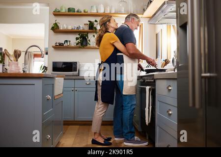 Liebe, Essen und ältere Paare kochen in einer Küche, umarmen und binden, während sie zusammen in ihrem Haus eine Mahlzeit zubereiten. Glückliche Familie, Ruhestand und reif Stockfoto