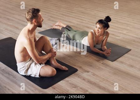Wir machten eine kleine Pause. Die ganze Aufnahme von zwei jungen Menschen, die eine Pause machen und sich unterhalten, während sie gemeinsam in einem Yoga-Studio arbeiten. Stockfoto