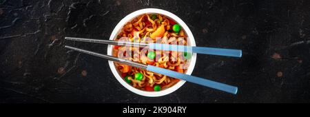 Ramen Tasse, Instant-Soba-Nudeln in einem Plastikbecher mit Gemüse und Essstäbchen Panorama, auf schwarzem Hintergrund Stockfoto