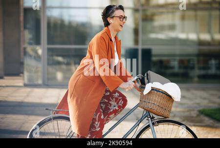 Fröhliche Geschäftsfrau, die am Morgen fröhlich lächelt, während sie mit dem Fahrrad zur Arbeit fährt. Reife Geschäftsfrau genießt ihr umweltfreundliches Büro pendeln ich Stockfoto