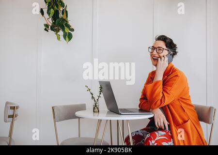 Glückliche, reife Geschäftsfrau, die während der Arbeit aus der Ferne telefoniert. Erfolgreiche Geschäftsfrau lächelt fröhlich während eines Telefongesprächens discussio Stockfoto