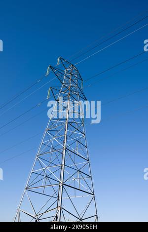 Ein Gitterübertragungsturm oder Pylon, der 132kv Stromkabel gegen einen klaren blauen Himmel transportiert. Stockfoto