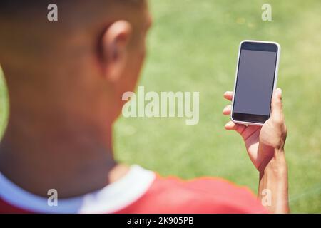 Mann, Fußballspieler und Telefon auf dem Feld mit Bildschirm, leer und Mockup im Internet. Mann, Fußballspieler und Smartphone in sozialen Medien, im Web oder in der App Stockfoto
