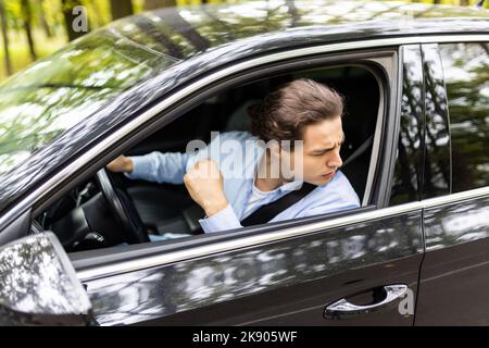 Verärgerter, müde junger Mann fährt mit dem Auto. Geschäftsmann kommt zu spät zu einem Treffen. Stockfoto