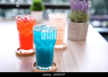 Erfrischendes kaltes Getränk für den Sommer auf Eis. Farbenfroher Sommerdrink in hohem Glas mit Holzuntertasse für heißen Tag und Party. Stockfoto