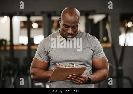 Schwarzer Mann, Zwischenablage und Schreiben in der Turnhalle für die Ausbildung Mitgliedschaft, melden Sie sich an oder Abonnement. Persönlicher Trainer, Checkliste und Mann aus Nigeria Holding Stockfoto
