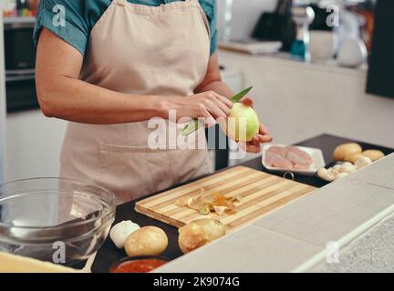 Das Aroma Zwiebeln in den Mahlzeiten ist jede Träne wert. Eine unkenntliche Frau schneiden eine Zwiebel beim Kochen in ihrer Küche zu Hause. Stockfoto