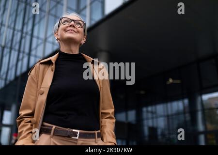 Porträt einer erfolgreichen erwachsenen charismatischen Führungspersönlichkeit vor dem Hintergrund einer Glasfassade eines Bürogebäudes, wirtschaftlich Stockfoto