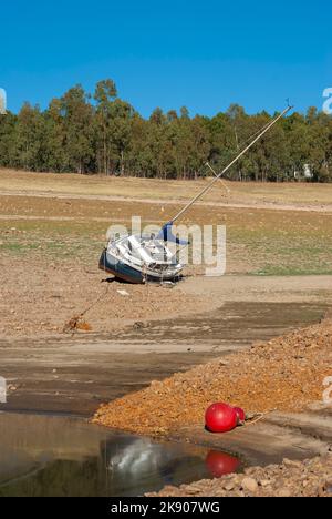 Segelboot gestrandet an Land wegen Dürre mit blauen Himmel Bäume im Hintergrund vertikal Stockfoto