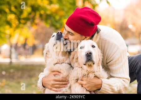 Glücklicher Mann mittleren Alters, der seine beiden Hunde, Golden Retriever, küsst. Freundschaft, Liebe und Fürsorge für Haustiere. Nahaufnahme. Stockfoto