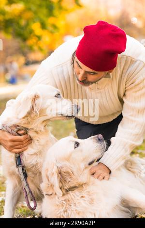 Mann mittleren Alters mit seinen beiden Hunden, Golden Retriever.Freundschaft, Liebe und Pflege für Haustiere. Nahaufnahme des vertikalen Fotos. Stockfoto