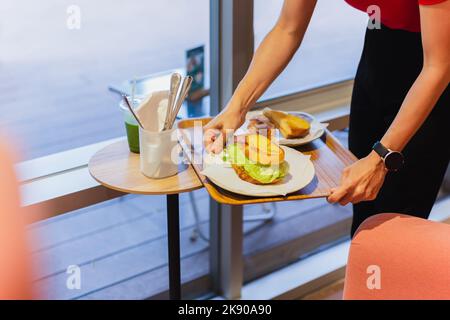 Kellnerin serviert Gemüsesandwich auf einem Tablett im Café. Stockfoto