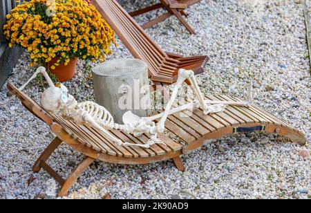 Menschliches Skelett, das sich auf einem Loungesessel im Freien auflehnend Stockfoto