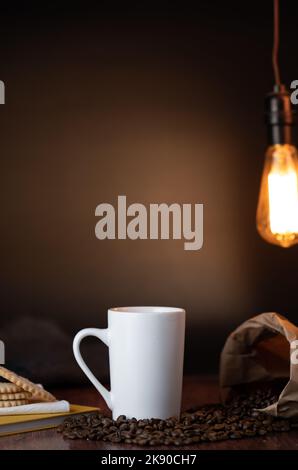 Ein weißer Kaffeebecher mit Kaffeebohnen in Papiertüte auf dunklem Hintergrund. Füge dem Becher dein eigenes Design hinzu. Stockfoto