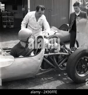 1962, historisch, ein Mann, der in einem einsitzigen Rennwagen sitzt und den Motor mit einem Mechaniker in Geoff Clarkes Motor Racing Stables, einer Fahrschule im Finmere Aerodome, einem stillgelegten RAF-Flugplatz in der Nähe von Buckingham, England, Großbritannien, ausgesetzt ist. Die 1.000-ccm-Einsitzer der Rennschule waren Formel-Junior-Coopers mit Heckmotor. Stockfoto