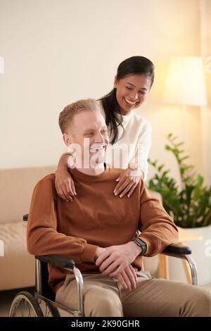 Lächelnde junge Frau, die sich um ihren Freund kümmert, der nach einem Autounfall gelähmt war Stockfoto