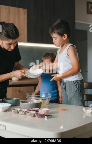 Junge, Mädchen und Mutter bereiten zu Hause Plätzchenteig, Muffins und Pfannkuchen zum Frühstück zu. Familie, Kochen, Backen und Menschen Konzept. Zeit mit der Familie Stockfoto