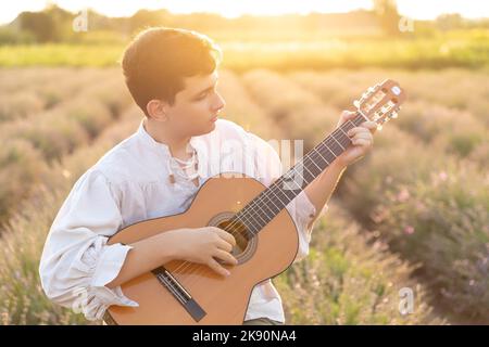 Der junge Mann spielt Gitarre im Lavendelfeld Stockfoto