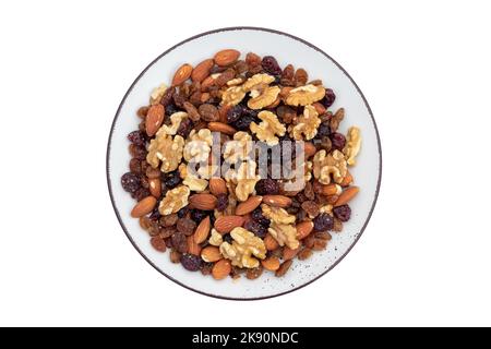 Gesunder Snack: Gemischte Nüsse und getrocknete Früchte in Keramikplatte isoliert auf weißem Hintergrund. Mandel, Walnuss, Preiselbeere, Rosine. Draufsicht. Vegetarische Kost Stockfoto