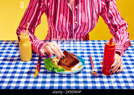 Mittagspause. Kreatives Porträt einer jungen Frau, die Kleidung im Vintage-Stil trägt, die bereit ist, Sandwich mit Salat und Orangensaft zu essen. Vintage-Retro-Style Stockfoto