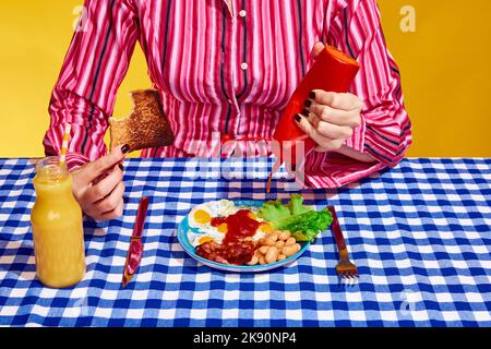 Kreatives Porträt einer jungen Frau, die Kleidung im Vintage-Stil trägt, die bereit ist, Sandwich mit Salat und Orangensaft zu essen. Interieur im Retro-Stil. Stockfoto