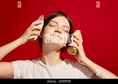 Melodie der mexikanischen Küche. Junges Mädchen, das Musik mit Tacos auf rotem Hintergrund hört. Vintage-Retro-Style. Food Pop Art Fotografie. Stockfoto