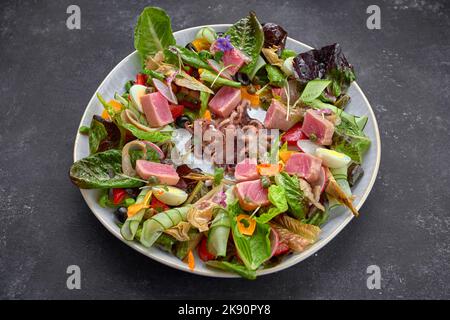 Salat mit Meeresfrüchten, Thunfisch und Tintenfisch auf einem Teller, auf dunklem Beton Stockfoto