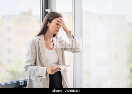 Eine kurze Aufnahme einer attraktiven Geschäftsfrau, die allein in ihrem Büro steht und unter Kopfschmerzen leidet. Stockfoto