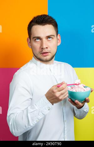 Ein Mann isst Marshmallows. Helles Männerporträt. Teller mit Süßigkeiten in den Händen eines Mannes Stockfoto
