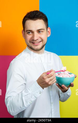 Ein Mann isst Marshmallows. Helles Männerporträt. Teller mit Süßigkeiten in den Händen eines Mannes Stockfoto