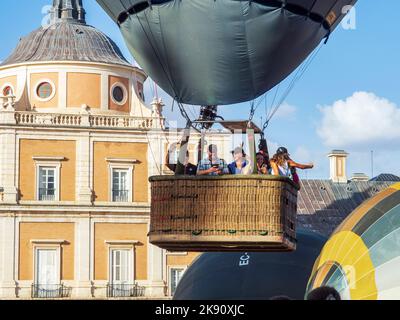 Ein Korb mit Passagieren eines Heißluftballons steigt mit dem Palast von Aranjuez im Hintergrund auf. Stockfoto