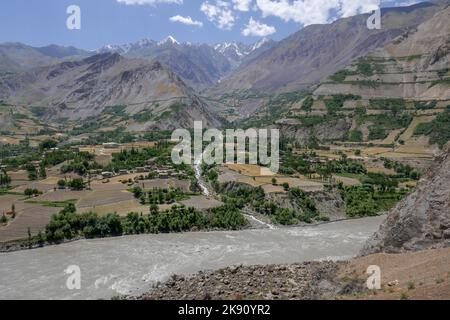 Malerisches Berglandschaftspanorama im Panj-Flusstal mit Bach und traditionellem Dorf auf afghanischer Seite, Darvaz, Gorno-Badakshan, Tadschikistan Pamir Stockfoto