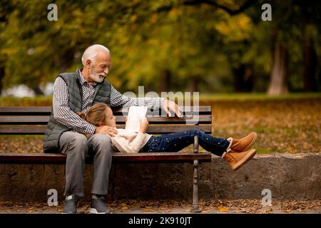 Der gutaussehende Großvater verbringt am Herbsttag Zeit mit seiner Enkelin auf der Bank im Park Stockfoto