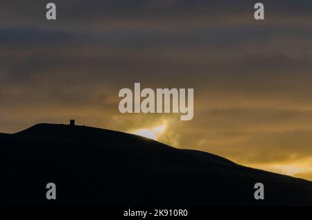 Herbstsonnenaufgang am Rivington Pike mit Hügel in Silhouette und Sonneneinstrahlung Wolken orange und gelb Stockfoto