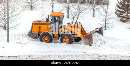 Schneeräumung. Der Traktor räumt nach starkem Schneefall den Weg frei. Ein großer orangefarbener Traktor entfernt Schnee von der Straße und räumt den Bürgersteig frei. Straßen reinigen Stockfoto