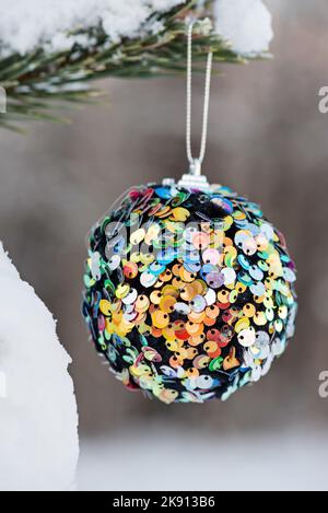 Aufgehängte bunte Glitzer Weihnachtskugel auf Fichte und über verschwommenem Hintergrund Stockfoto
