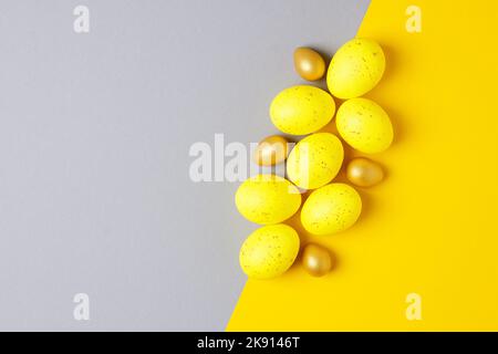 Ostereier in Gelb und Gold auf gelbem und grauem Hintergrund. Flach liegend, Kopierplatz. Stockfoto