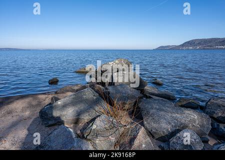 Felsbrocken als Teil eines Wellenbrechers in einem See. Bild vom See Vattern, Schweden. Blaues Wasser und Himmel im Hintergrund Stockfoto