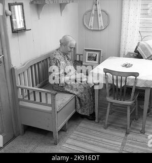 In der 1950s. Eine ältere Dame wird in ihrer Küche gesehen, die auf einem hölzernen Sofa sitzt und Kaffee trinkt. Schweden 1953 Conard Ref. 2489 Stockfoto