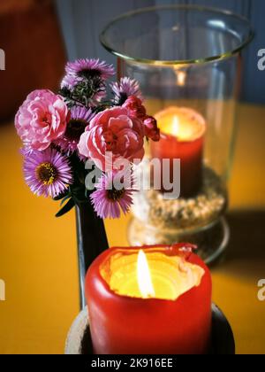 Der Garten blüht Aster und Rosen in einer Vase neben roten Kerzen eine davon im Vakuum Stockfoto