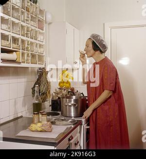 In der Küche 1960s. Das Innere einer Küche und eine Frau, die am Herd steht und etwas von den Töpfen und Pfannen schmeckte. Sie hat das Haarnetz an, um zu verhindern, dass Haare in die Nahrung fallen. Schweden 1962 Ref. cv83 Stockfoto