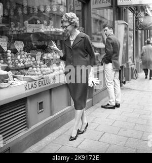 In der 1950s. Eine Frau wird auf der Straße und im Schaufenster eines Obst- und Lebensmittelgeschäfts abgebildet. Sie sieht so aus, als würde sie entscheiden, was sie kaufen soll. In passender Jacke und Rock. Schweden 1959 Kristoffersson Ref. CF58-4 Stockfoto