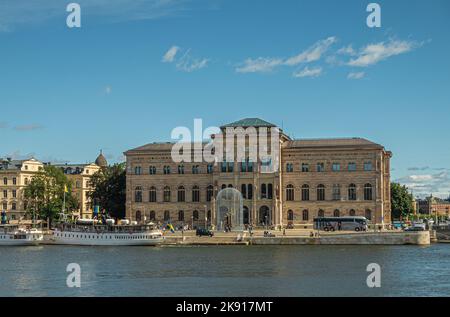 Schweden, Stockholm - 17. Juli 2022: Skeppsbron Kai. Nationalmuseum unter blauer Wolkenlandschaft. Kleine Boote im Hafen- und Stadtbild Stockfoto