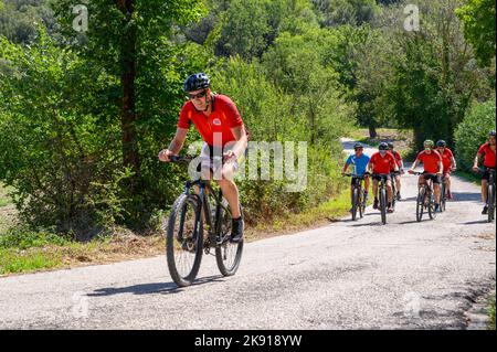 Eine Gruppe norwegischer Radfahrer mittleren Alters mit gemieteten Fahrrädern durchquert eine hügelige Straße in der umbrischen Landschaft in der Nähe von Spoleto, Umbrien, Italien. Stockfoto