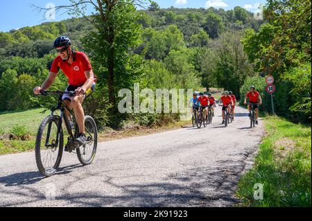 Eine Gruppe norwegischer Radfahrer mittleren Alters mit gemieteten Fahrrädern durchquert eine hügelige Straße in der umbrischen Landschaft in der Nähe von Spoleto, Umbrien, Italien. Stockfoto