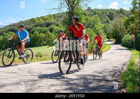 Eine Gruppe norwegischer Radfahrer mittleren Alters mit gemieteten Fahrrädern durchquert eine hügelige Straße in der umbrischen Landschaft in der Nähe von Spoleto, Umbrien, Italien. Stockfoto