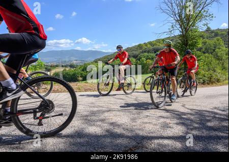 Eine Gruppe norwegischer Radfahrer mittleren Alters mit gemieteten Fahrrädern durchquert eine hügelige Straße in der umbrischen Landschaft in der Nähe von Spoleto, Umbrien, Italien. Stockfoto